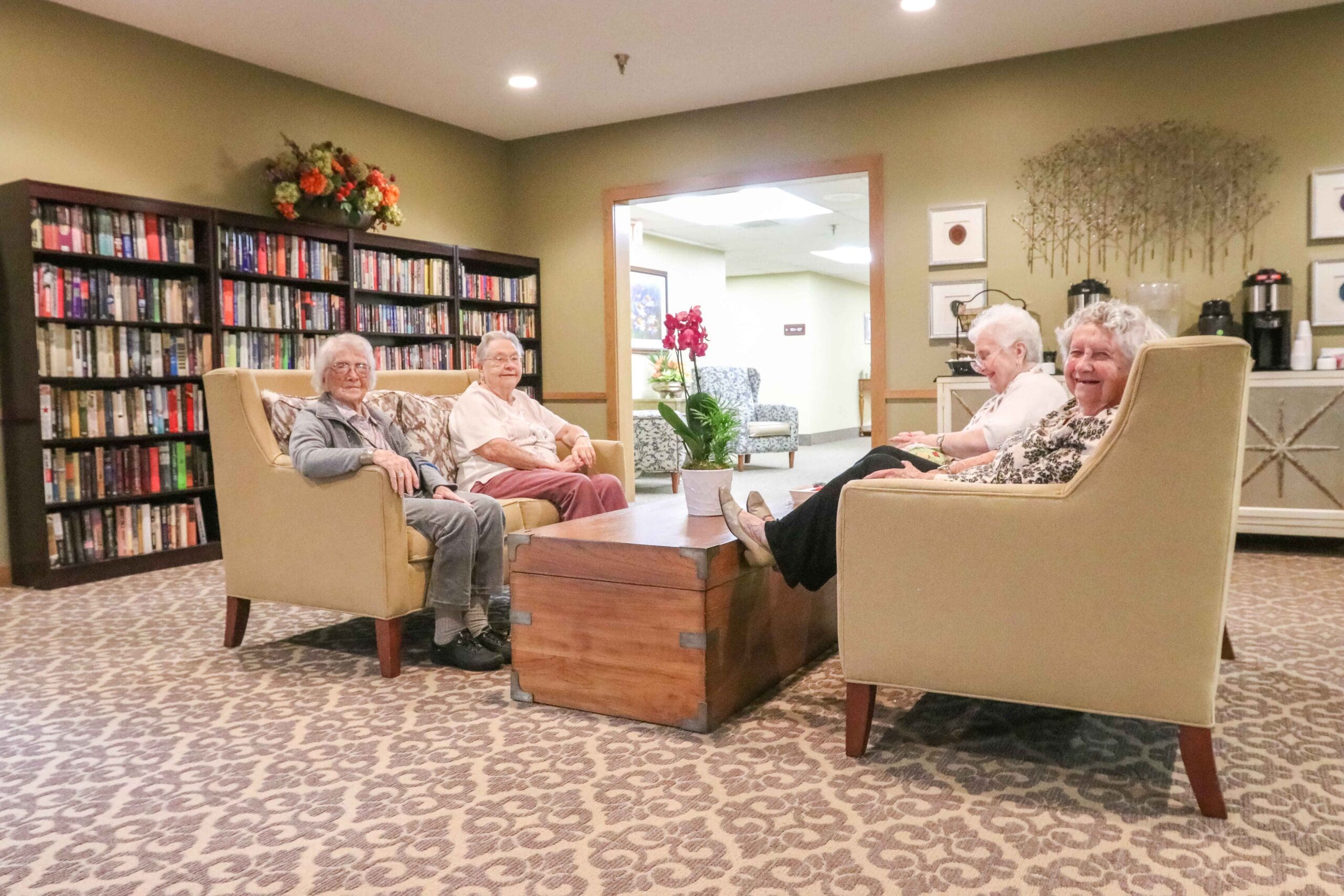 Residents sit in the common area, enjoying comfortable chairs, a library, and free coffee services at Inspirations at Bartlesville.