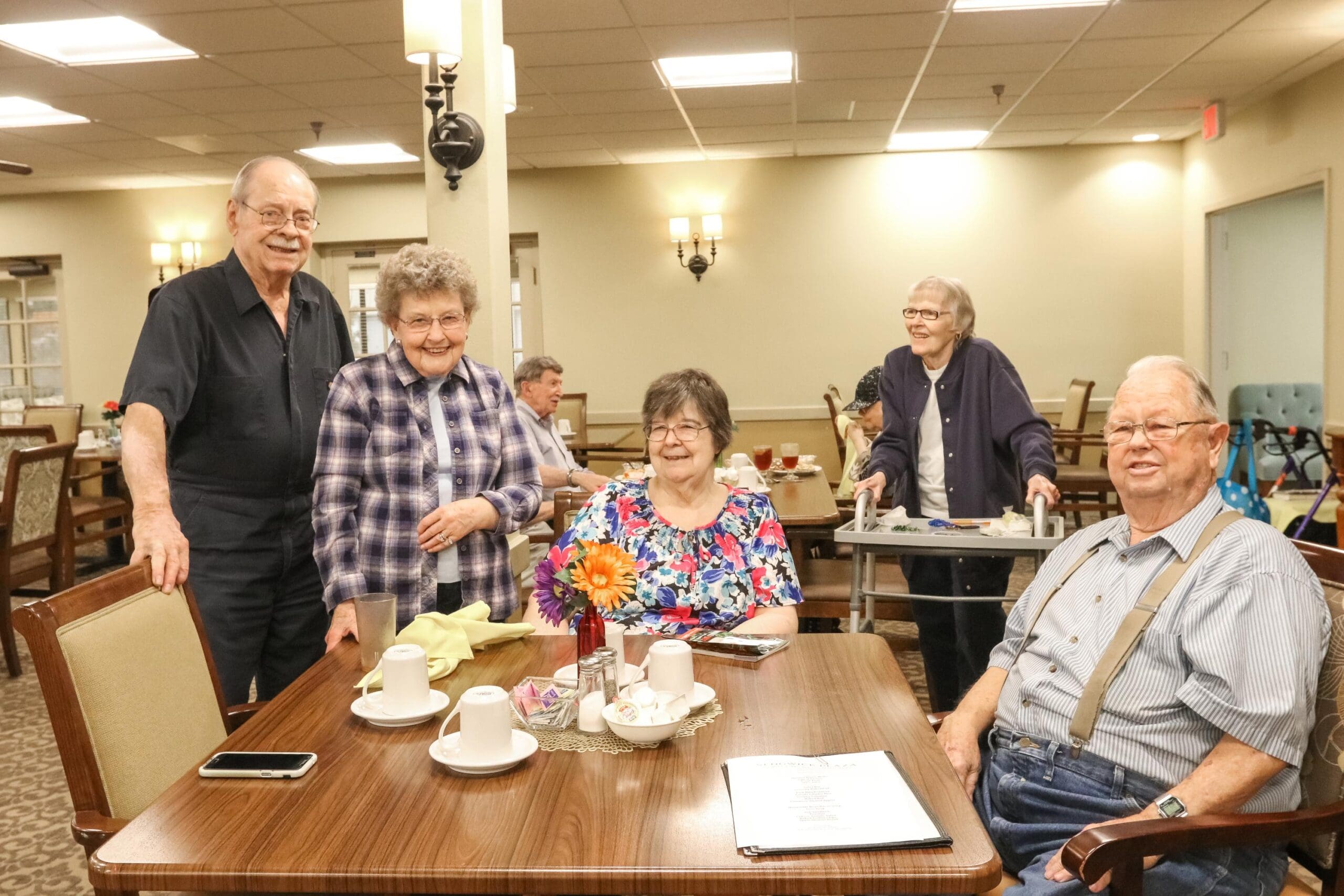 Residents standing around a dining table together in the dining room at Inspirations of Bartlesville.