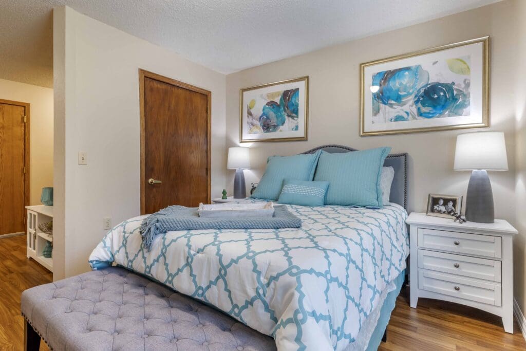 Interior image of a resident's bedroom with a blue and white made bed at Inspirations of Bartlesville.